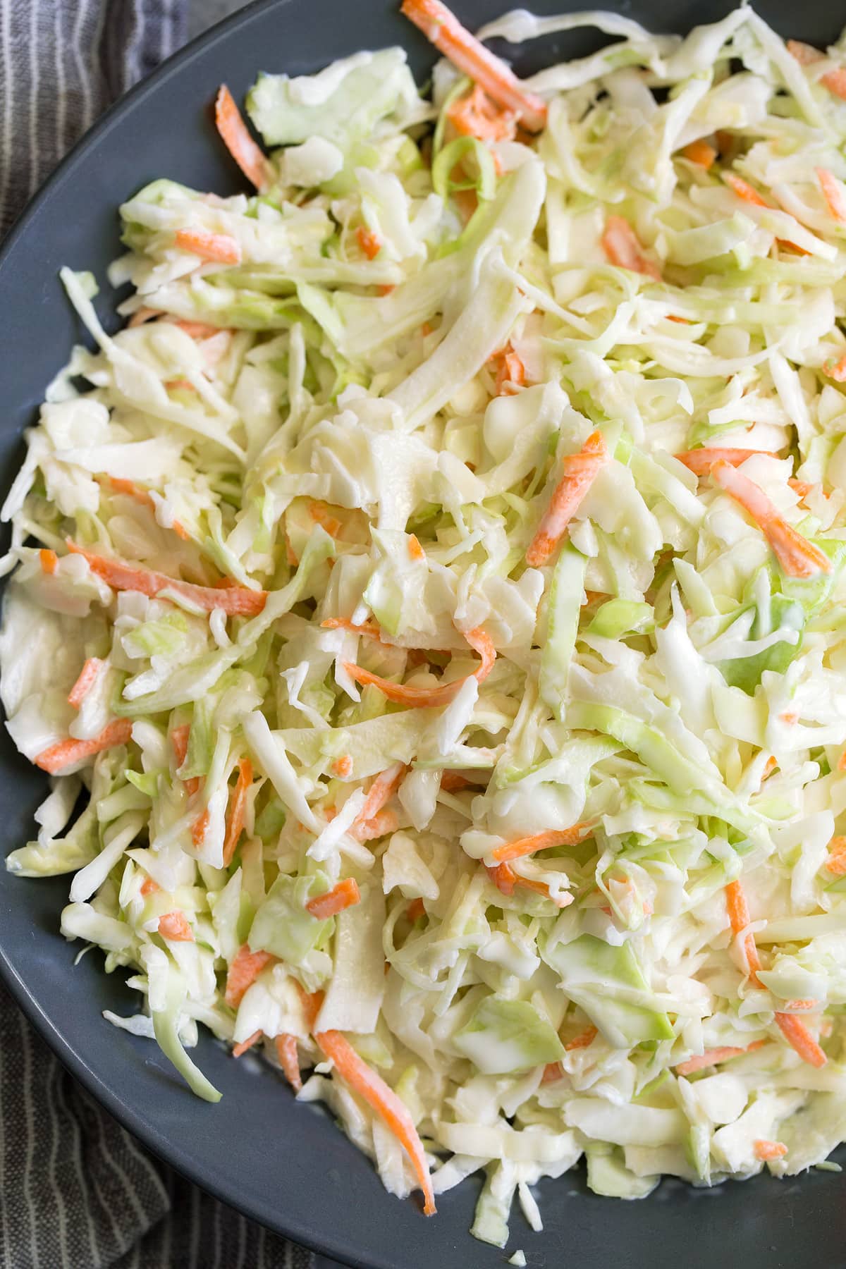Recette de salade de chou Close up image de salade de chou avec vinaigrette dans un bol bleu foncé.
