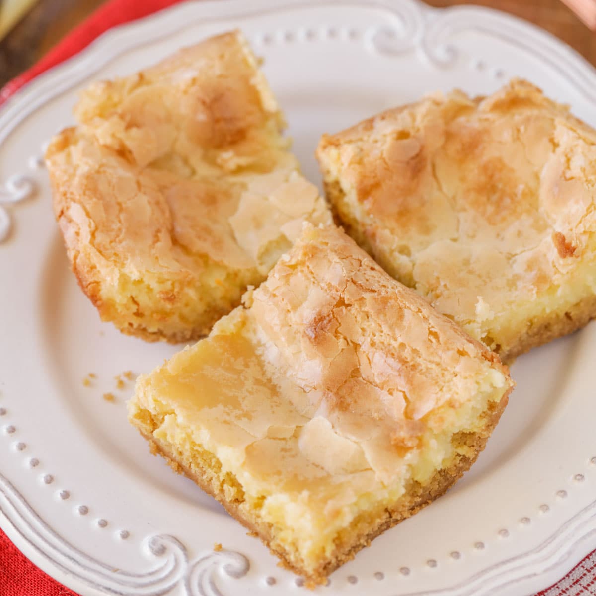 Le gâteau au beurre gluant est un dessert simple et incroyablement délicieux avec une croûte de pâte à gâteau et un dessus de fromage à la crème doux et gluant qui le rend addictif! Trois tranches de gâteau au beurre gluant sur une plaque blanche