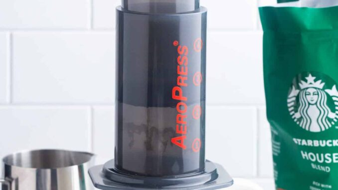 a female hand with red nails, using an aeropress to make a cup of coffee.