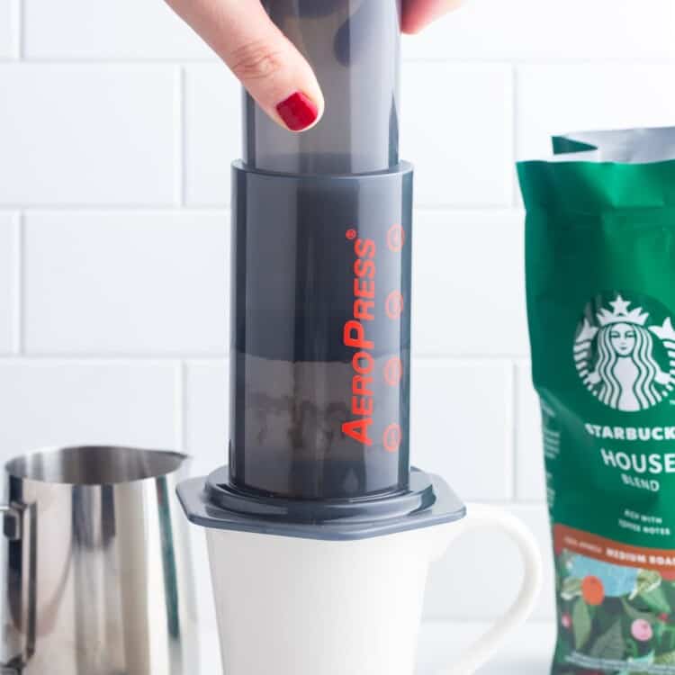 une main féminine avec des ongles rouges, utilisant un aeropress pour faire une tasse de café.