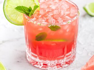 pink drink in short glass with mint inside garnished with a lime wheel and sprig of mint
