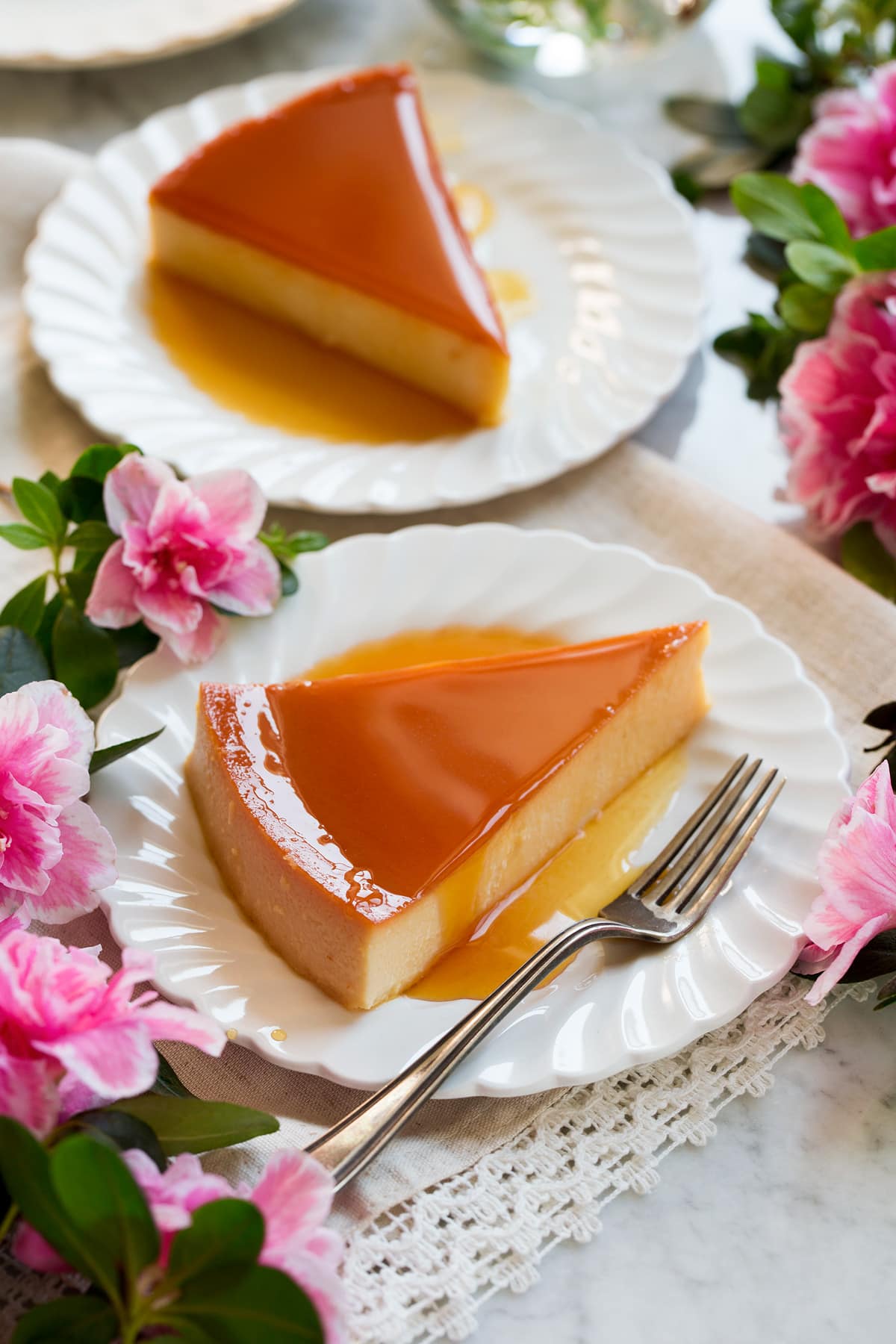 Recette de flans Image de deux tranches de flan sur des assiettes festonnées blanches avec des fleurs sur les côtés.