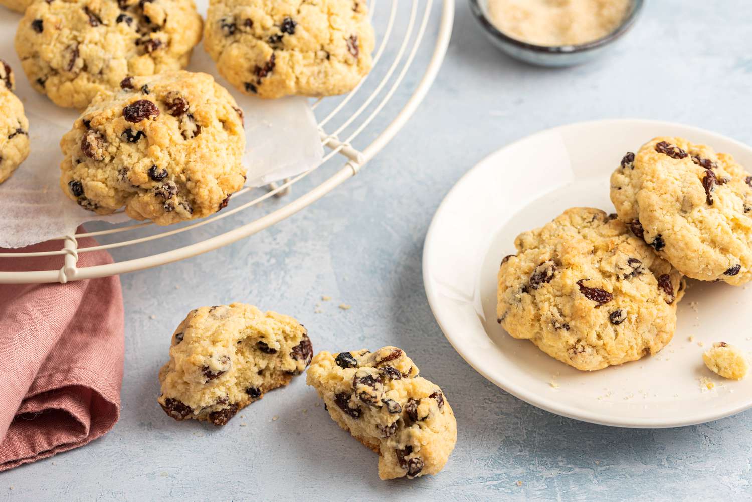 Lightly browned rock cakes studded with raisins on a plate and on a wire cooling rack