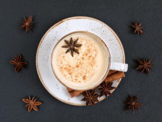 overhead view of chai tea in a white mug on a saucer on a dark slate background surrounded by spices