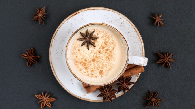 overhead view of chai tea in a white mug on a saucer on a dark slate background surrounded by spices